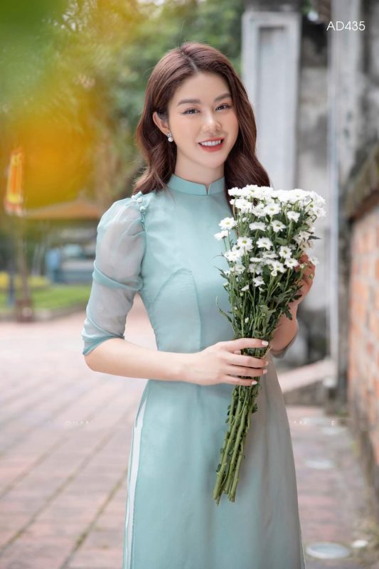 Áo dài cưới là trang phục không thể thiếu trong ngày trọng đại của phụ nữ Việt Nam. Tuy nhiên, cùng với sự phát triển của thời trang, chiếc áo dài cưới truyền thống đã được nâng tầm thành phiên bản áo dài cưới cách tân – một lựa chọn hoàn hảo cho những cô dâu yêu thích sự tinh tế, độc đáo nhưng vẫn giữ trọn vẹn nét duyên dáng, thanh lịch. Áo dài cách tân không chỉ mang lại sự thoải mái, tiện lợi mà còn là tuyên ngôn thời trang mạnh mẽ, giúp cô dâu tỏa sáng rạng rỡ nhất trong hôn lễ. Vì Sao Áo Dài Cưới Cách Tân Lên Ngôi? Sự nổi lên của áo dài cách tân không phải là ngẫu nhiên. Nó đáp ứng hoàn hảo nhu cầu của cô dâu hiện đại, người mong muốn một trang phục cưới linh hoạt hơn mà vẫn giữ được giá trị văn hóa. 1. Thoải Mái và Tiện Lợi: Điểm cộng lớn nhất của áo dài cách tân là sự thoải mái. Thay vì cổ cao truyền thống, áo dài cách tân thường sử dụng các kiểu cổ đa dạng như cổ thuyền, cổ tròn, cổ V hay thậm chí là cổ yếm, giúp cô dâu dễ thở và khoe khéo xương quai xanh quyến rũ. Phần tay áo cũng được biến tấu thành tay lỡ, tay phồng hoặc tay bồng, tạo sự trẻ trung và năng động, thuận tiện hơn cho việc di chuyển, đón khách trong suốt buổi tiệc. 2. Đa Dạng Trong Thiết Kế và Chất Liệu: Nếu áo dài truyền thống bị giới hạn về chất liệu và phom dáng, áo dài cách tân mở ra cánh cửa sáng tạo vô tận. Cô dâu có thể lựa chọn các loại vải hiện đại hơn như Voan, Organza, Taffeta, kết hợp với các kỹ thuật thủ công tinh xảo như đính kết 3D, thêu chỉ ánh kim, hay sử dụng kỹ thuật cắt may hiện đại để tạo ra các chi tiết xếp ly, nhún bèo độc đáo ở vai, eo hoặc tà áo. 3. Phù Hợp Với Mọi Vóc Dáng và Địa Điểm Cưới: Nhờ sự linh hoạt trong thiết kế, áo dài cách tân có thể "chiều lòng" mọi vóc dáng. Tà áo được biến tấu thành tà ngắn ngang gối, tà lửng, hoặc tà kép với độ bồng bềnh nhẹ, giúp cô dâu có chiều cao khiêm tốn trông thanh thoát hơn, đồng thời phù hợp với cả tiệc cưới ngoài trời, bãi biển hay không gian nhà hàng sang trọng. Những Xu Hướng Áo Dài Cưới Cách Tân Đang Được Yêu Thích Thị trường áo dài cưới cách tân luôn sôi động với những ý tưởng mới mẻ. Dưới đây là ba xu hướng nổi bật nhất mà cô dâu không thể bỏ qua: 1. Áo Dài Tà Kép và Tay Bồng (Tà Phồng): Đây là sự kết hợp hoàn hảo giữa nét kiêu sa của váy cưới phương Tây và sự dịu dàng của áo dài Việt Nam. Tà áo dài được may hai lớp, lớp trong bằng lụa mỏng ôm sát, lớp ngoài bằng Voan hoặc Organza tạo độ phồng nhẹ. Tay bồng hoặc tay phồng nhẹ nhàng ở vai giúp cô dâu có bờ vai thon gọn và tăng thêm vẻ lãng mạn, cổ tích. 2. Áo Dài Kết Hợp Họa Tiết Hiện Đại và Màu Sắc Táo Bạo: Không chỉ giới hạn ở các màu đỏ, trắng, vàng truyền thống, áo dài cách tân hiện đại còn sử dụng các tông màu pastel (xanh ngọc, hồng đất) hoặc màu sắc đậm (xanh navy, tím than) để tạo sự khác biệt. Họa tiết được ứng dụng là các mảng thêu, đính kết pha lê theo phong cách tối giản, hoặc hình khối hiện đại thay vì rồng phượng cầu kỳ như trước, tạo cảm giác tinh tế và sang trọng. 3. Áo Dài Cổ Yếm/Cổ Thuyền Kết Hợp Quần Culottes/Chân Váy: Đối với cô dâu muốn sự đột phá, áo dài cưới cách tân còn được kết hợp cùng quần Culottes (ống rộng) hoặc chân váy xòe/chân váy chữ A, thay thế cho chiếc quần lụa bó sát truyền thống. Sự kết hợp này mang đến vẻ ngoài cực kỳ thời thượng, tiện dụng như một bộ đầm dạ hội mà vẫn giữ được kiểu dáng thân áo dài duyên dáng. Áo dài cổ yếm hoặc cổ thuyền khoe trọn vẻ đẹp của cổ và vai, đặc biệt phù hợp với cô dâu có phong cách gợi cảm, phóng khoáng. Bí Quyết Lựa Chọn Áo Dài Cưới Cách Tân Chuẩn Nhất Cho Cô Dâu Để chiếc áo dài cách tân thật sự hoàn hảo, cô dâu cần lưu ý những điểm sau trong quá trình lựa chọn và đặt may: 1. Chọn Kiểu Dáng Phù Hợp Với Dáng Người: Dáng người tròn, đầy đặn: Nên chọn áo dài có chất liệu đứng form như Gấm, Taffeta, tránh các chất liệu quá mỏng hoặc bóng. Ưu tiên cổ V hoặc cổ tim để tạo cảm giác thon gọn. Dáng người gầy, cao: Thích hợp với các kiểu áo dài có tà bồng, tay phồng, và có thể chọn chất liệu có độ bóng như Lụa để tạo cảm giác đầy đặn hơn. Dáng người quả lê (hông lớn): Chọn áo dài có tà xòe nhẹ, độ dài tà phủ mắt cá chân để cân đối lại tỷ lệ cơ thể. 2. Ưu Tiên Sự Hài Hòa Của Tổng Thể: Dù là cách tân, cô dâu vẫn cần đảm bảo sự hài hòa với trang phục của chú rể và tổng thể phong cách tiệc cưới. Nếu tiệc cưới theo phong cách Vintage, nên chọn áo dài cách tân với màu sắc trầm ấm, họa tiết ren hoặc thêu tay cổ điển. Nếu tiệc cưới hiện đại, hãy mạnh dạn chọn màu sắc tươi sáng và họa tiết 3D nổi bật. 3. Chất Lượng Vải và Kỹ Thuật May: Chất liệu là yếu tố quyết định sự sang trọng của chiếc áo dài. Hãy chọn studio, nhà may uy tín, nơi sử dụng chất liệu nhập khẩu, kỹ thuật cắt may chính xác và tay nghề thợ thêu, đính kết cao cấp. Một chiếc áo dài cách tân đẹp không chỉ nằm ở kiểu dáng mà còn ở độ rũ, độ đứng form và sự thoải mái khi mặc. 4. Đừng Quên Phụ Kiện Đi Kèm: Phụ kiện đi kèm áo dài cách tân cũng nên được tối giản hóa. Thay vì mấn truyền thống, cô dâu có thể sử dụng cài tóc, vương miện nhỏ hoặc khăn voan ngắn, kết hợp với giày cao gót mũi nhọn đơn giản để tôn lên nét hiện đại, thanh thoát của trang phục. Tương Lai Của Áo Dài Cưới Cách Tân Áo dài cưới cách tân không chỉ là một xu hướng nhất thời mà còn là minh chứng cho thấy trang phục truyền thống có thể thích nghi và phát triển cùng thời đại. Với sự sáng tạo không ngừng nghỉ của các nhà thiết kế Việt Nam, áo dài cách tân chắc chắn sẽ tiếp tục là nguồn cảm hứng bất tận, mang đến những kiệt tác thời trang cưới độc đáo, giúp mỗi cô dâu Việt Nam tự tin, kiêu hãnh và thật sự lộng lẫy trong ngày hạnh phúc nhất đời mình. Lựa chọn áo dài cưới cách tân là lựa chọn sự giao thoa hoàn hảo giữa quá khứ và hiện tại, tôn vinh vẻ đẹp truyền thống mà không hề lạc hậu, giúp cô dâu tạo nên dấu ấn cá nhân khó quên.